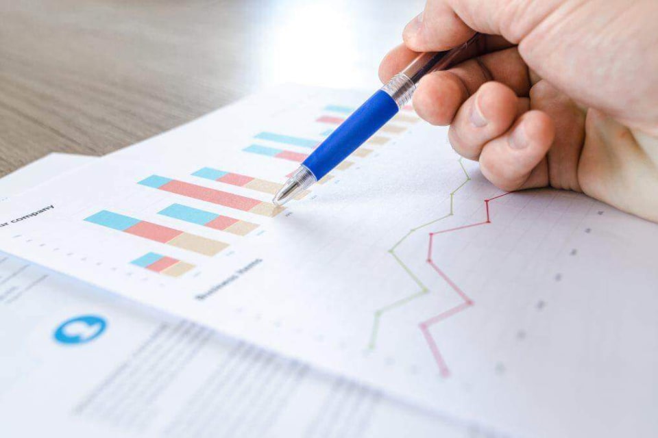 Hand with a pen pointing to a stack of statistics on paper