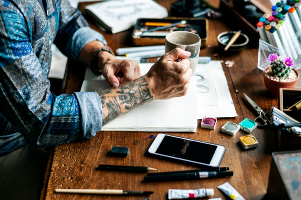 Tattooed man sitting at a work desk next to a phone