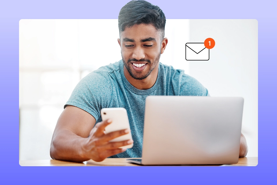 Man in front of his laptop looking at his phone reading about email marketing trends
