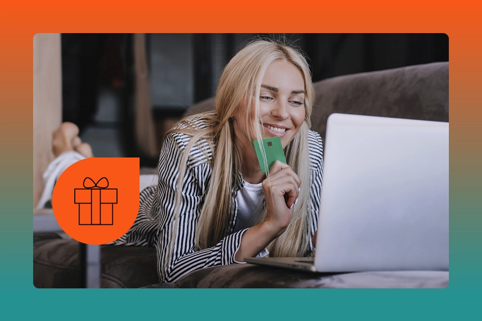 Woman with a credit card smiling at a laptop next to an icon of a present