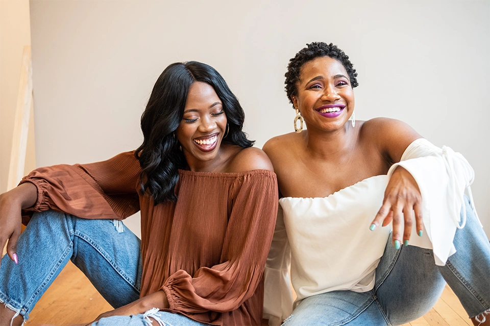 two women laughing as they sit on the floor