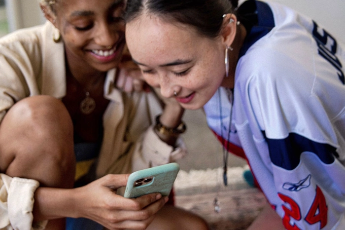 Two women on looking at a phone, an example of an audience brands can use to leverage social media