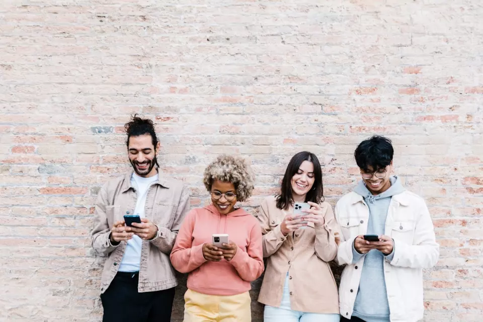 Four people leaning against a brick wall looking at their phones